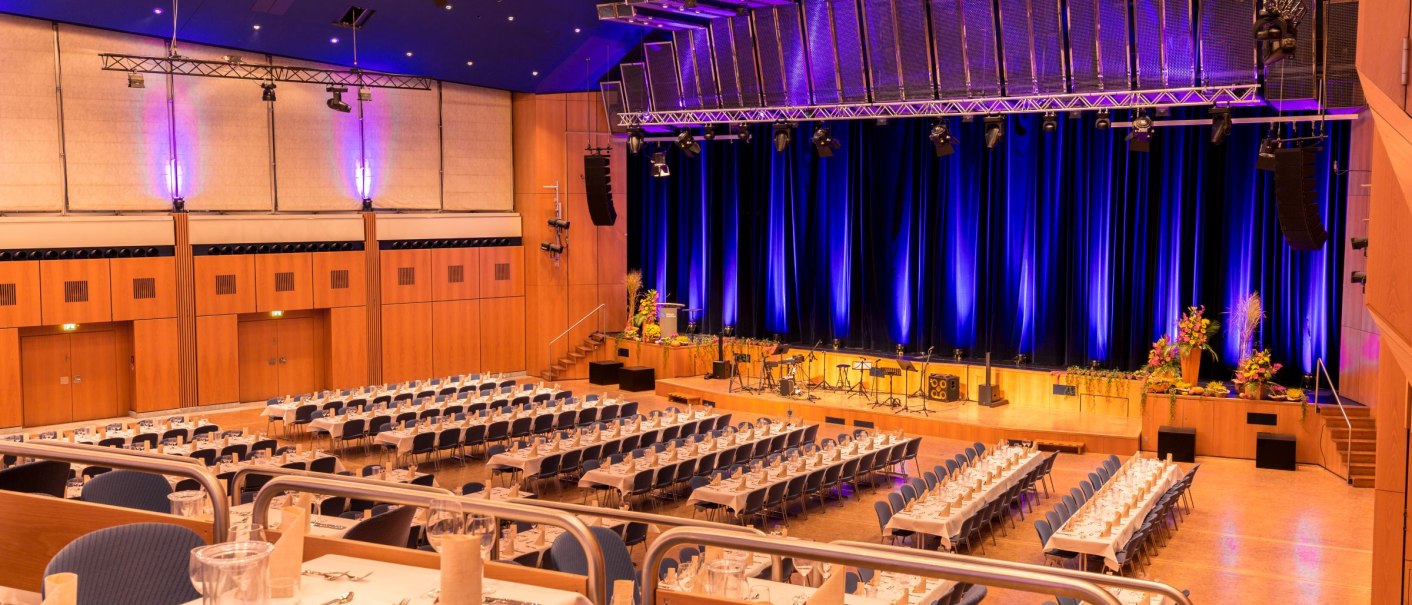 Großer Saal der Stadthalle Sindelfingen, festlich gedeckte Tische, Bühne mit blauer Beleuchtung, bereit für eine Veranstaltung., © ccbs