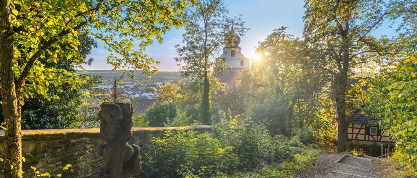 A sunny park path with trees, a statue and a building in the background. The sun shines through the leaves., © Stuttgart Marketing GmbH, Fotografin Martina Denker