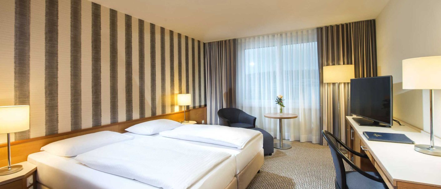 Modern hotel room with double bed, desk, TV and armchair. Subtle striped patterns on the wall and neutral colors dominate the design., &copy; Maritim Hotelgesellschaft mbH
