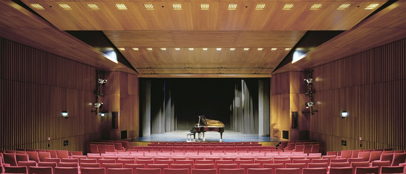 Theater hall with red seats, wooden walls and a grand piano on the stage. The lighting is warm and evenly distributed., © © Brigida González, Stuttgart Theater hall with red seats, wooden walls and a grand piano on the stage. The lighting is warm and evenly distributed., © © Brigida González, Stuttgart
