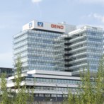 Das GENO-Haus mit moderner Glasfassade und mehreren Stockwerken, umgeben von Bäumen, unter einem blauen Himmel., © Geno-Haus Das GENO-Haus mit moderner Glasfassade und mehreren Stockwerken, umgeben von Bäumen, unter einem blauen Himmel., © Geno-Haus