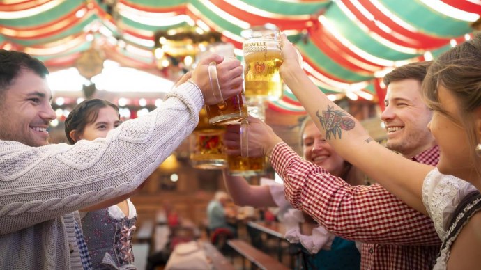 Menschen in traditioneller Kleidung sto&szlig;en mit Bierkr&uuml;gen in einem festlich dekorierten Zelt an. Fr&ouml;hliche Stimmung auf einem Volksfest., &copy; Stuttgart-Marketing GmbH, Sarah Schmid