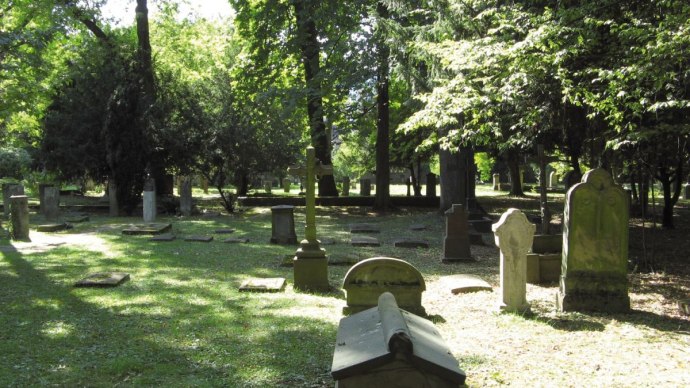 Gräber auf dem Hoppenlaufriedhof, umgeben von Bäumen. Sonnenlicht fällt durch das Blätterdach und beleuchtet die Grabsteine und den Boden., © Stuttgart-Marketing GmbH Gräber auf dem Hoppenlaufriedhof, umgeben von Bäumen. Sonnenlicht fällt durch das Blätterdach und beleuchtet die Grabsteine und den Boden., © Stuttgart-Marketing GmbH