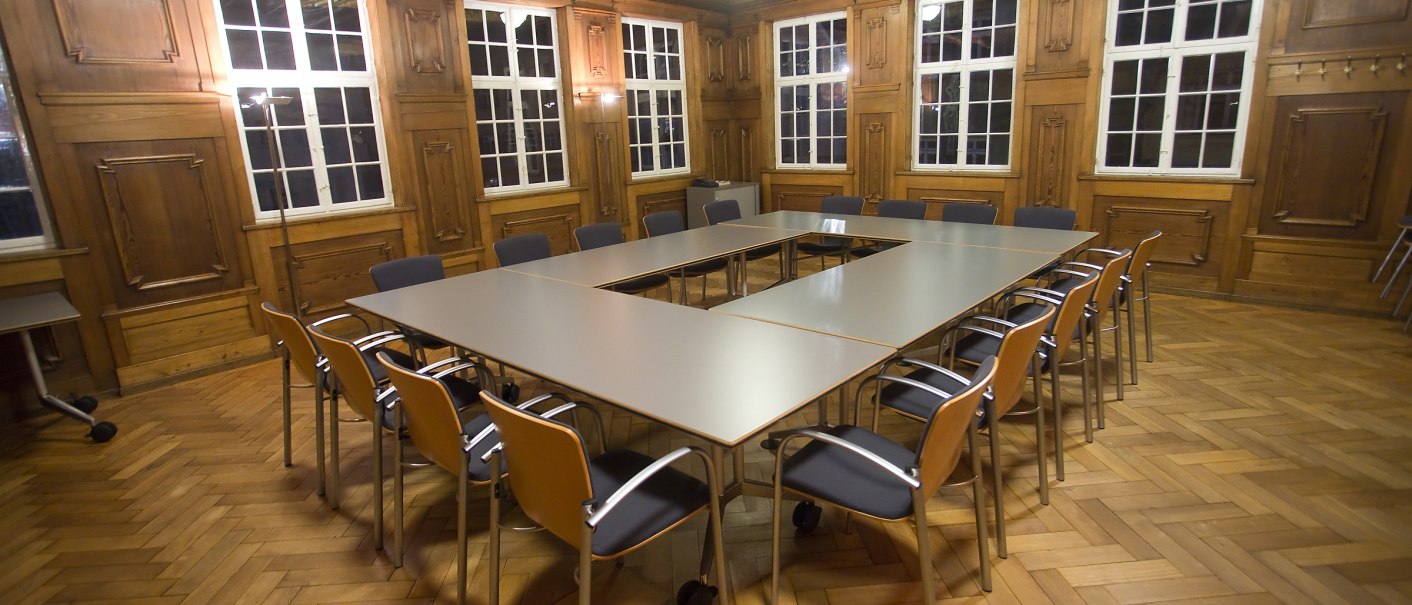 A conference room with wood paneling, large windows and a U-shaped table surrounded by chairs on a parquet floor., &copy; Esslingen live