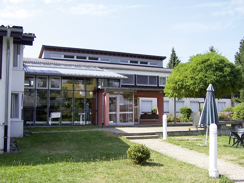 Modern building with a glass façade, surrounded by green spaces and a sunshade. Clear lines and large windows characterize the architecture., © L