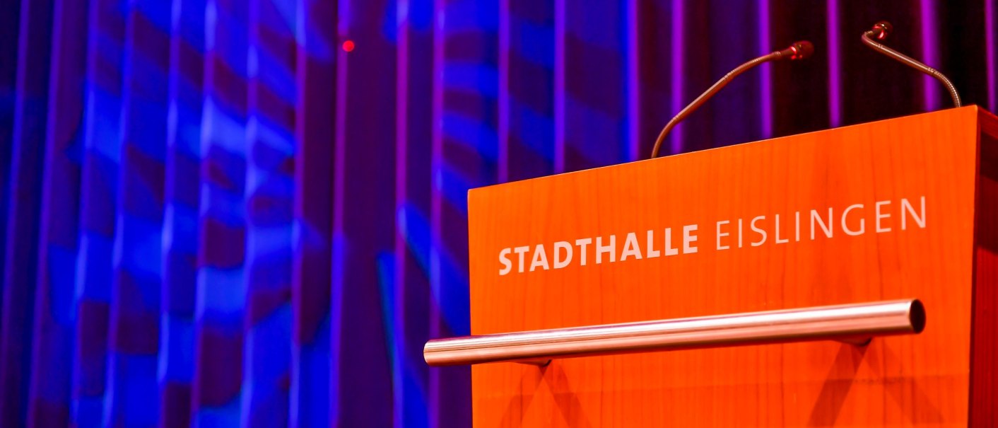 Ein Rednerpult mit der Aufschrift 'Stadthalle Eislingen' vor einem blau beleuchteten Vorhang., © GIACINTO_CARLUCCI