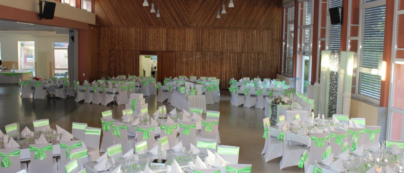 Ein festlich dekorierter Saal mit weiß-grünen Stühlen und Tischen, bereit für eine Feier in der Festhalle Althütte., © Gemeinde Althütte