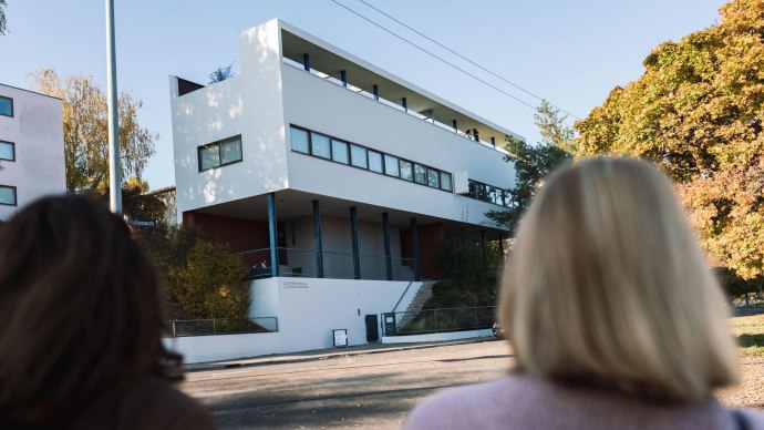 Two people look at the Le Corbusier house in the Weißenhofsiedlung. Modern building with clear lines, surrounded by autumnal trees., © Stuttgart-Marketing GmbH, wpsteinheisser