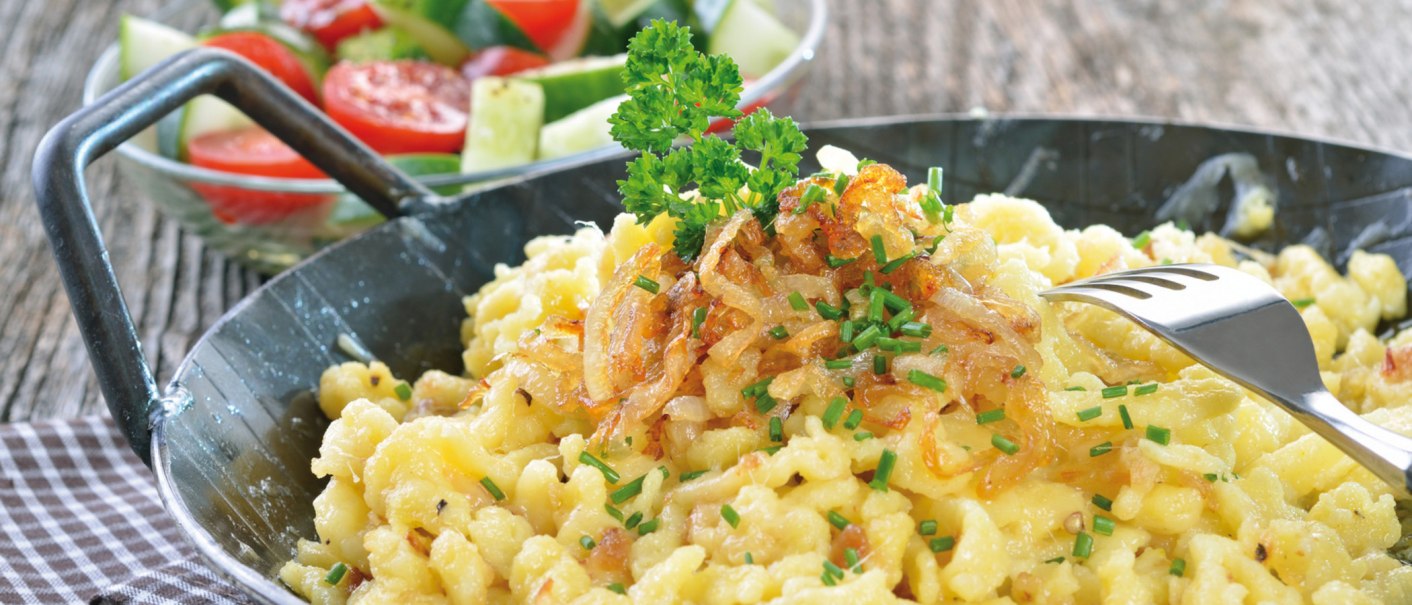 Käsespätzle mit Röstzwiebeln und Schnittlauch in einer Pfanne, daneben ein frischer Salat mit Tomaten und Gurken., © kab-vision - Fotolia
