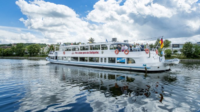 Das Passagierschiff MS Wilhelma f&auml;hrt auf einem Fluss. Der Himmel ist blau mit Wolken. Menschen stehen an Bord, und eine deutsche Flagge weht am Heck., &copy; all copyrights are reserved by maks richter