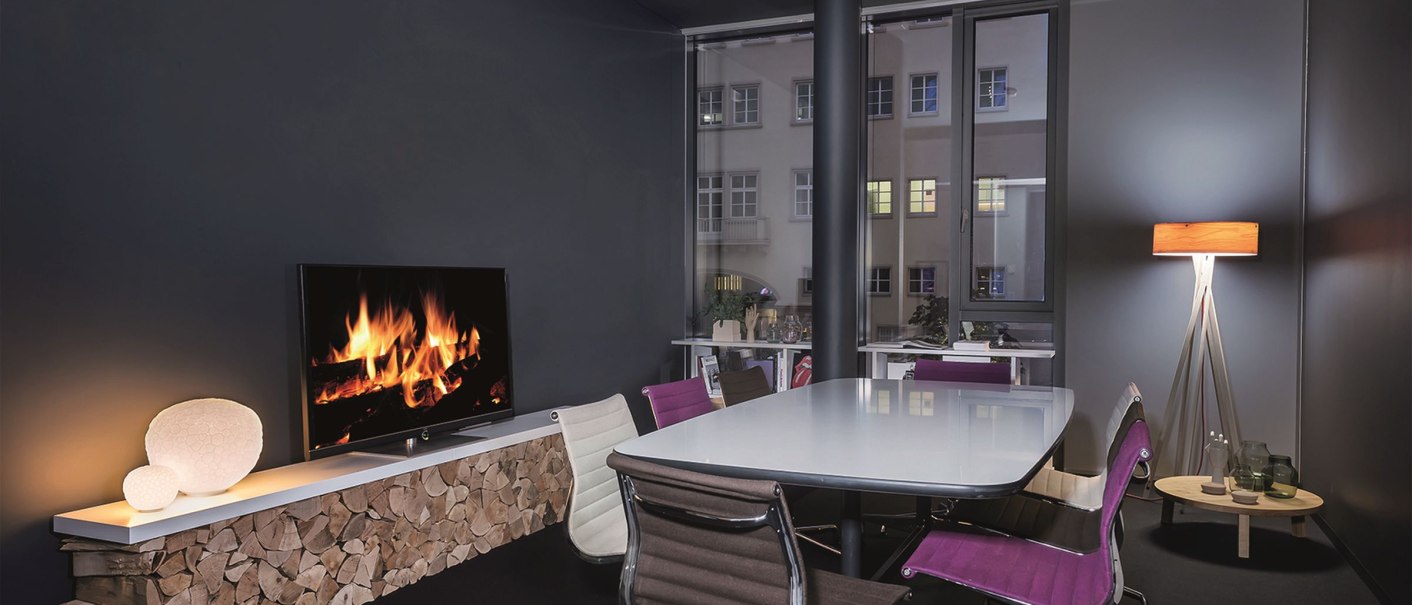 Moderner Konferenzraum mit Kaminbildschirm, weißem Tisch und bunten Stühlen. Große Fenster und stilvolle Beleuchtung schaffen eine gemütliche Atmosphäre., © Design Offices GmbH Moderner Konferenzraum mit Kaminbildschirm, weißem Tisch und bunten Stühlen. Große Fenster und stilvolle Beleuchtung schaffen eine gemütliche Atmosphäre., © Design Offices GmbH