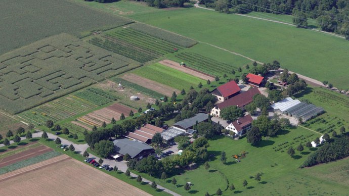 Luftaufnahme eines Bauernhofs mit mehreren Geb&auml;uden, Gew&auml;chsh&auml;usern und Feldern. Ein Labyrinth ist in einem Feld zu erkennen., &copy; Sonnenhof GmbH & Co KG