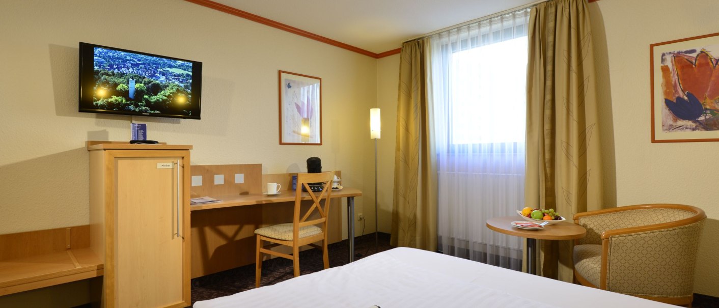 Comfortable hotel room with double bed, desk, TV, armchair and table with fruit. Light curtains and warm colors dominate the room., &copy; DH STUDIO Dirk Holst