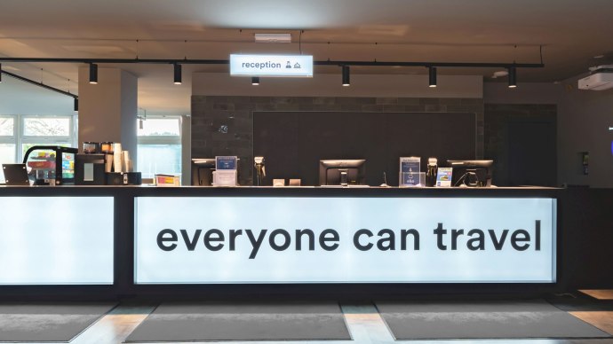 Modern reception at the a&o Stuttgart City with illuminated counter and the slogan 'everyone can travel'., &copy; a&o Hostels