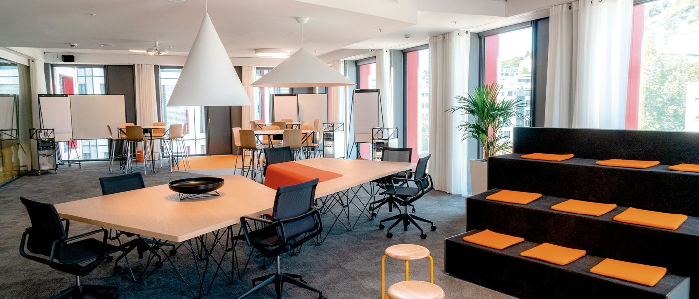 Modern work area with tables, chairs, seating steps and plants. Large windows let in plenty of light. Bright and friendly atmosphere., © INFOMOTION