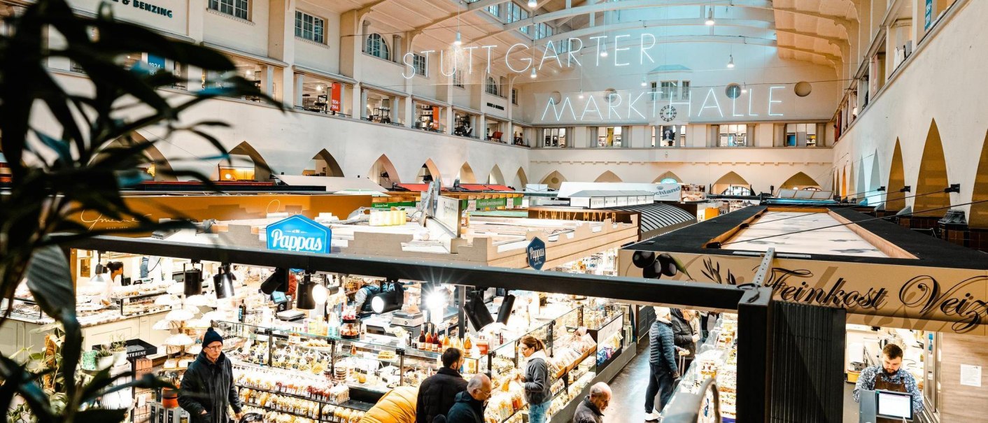 Blick von der Empore in die Stuttgarter Markthalle. Zahlreiche Stände und Besucher sind zu sehen, beleuchtet von hellem Licht., © Stuttgart Marketing GmbH, Sarah Schmid