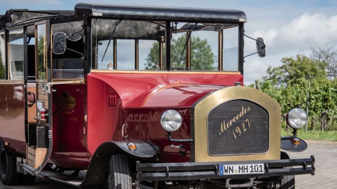 Roter Cabrio-Oldtimerbus mit Mercedes-Logo, Baujahr 1927, auf gepflastertem Weg vor grüner Landschaft., © Stuttgart-Marketing GmbH, trickytine