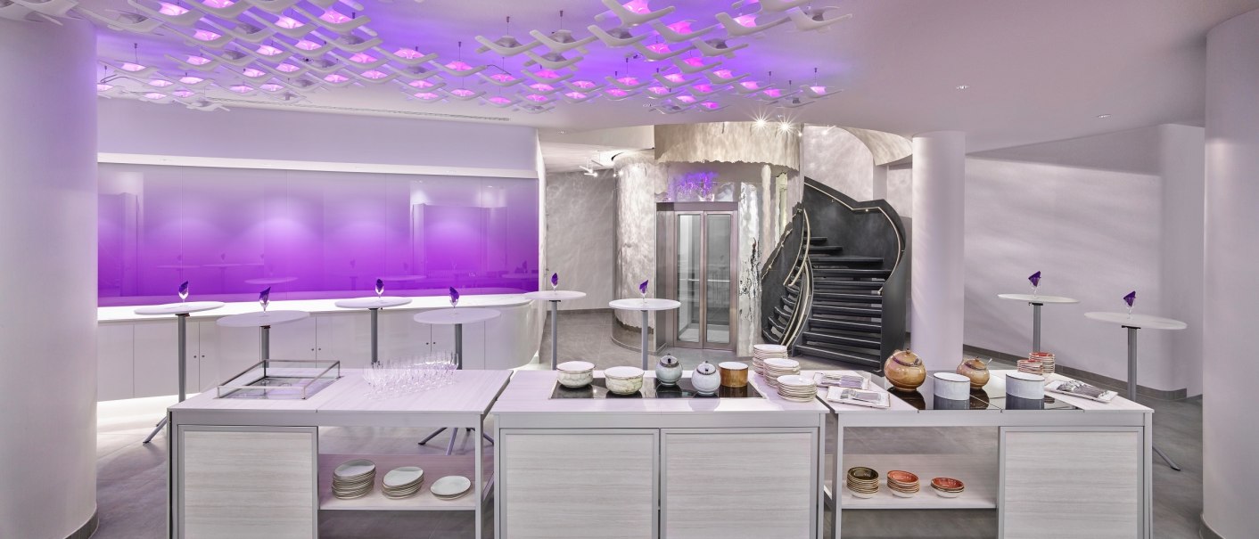 Modern room with purple lighting, round tables and stairs. Crockery and glasses on a table in the foreground., &copy; JazHotels