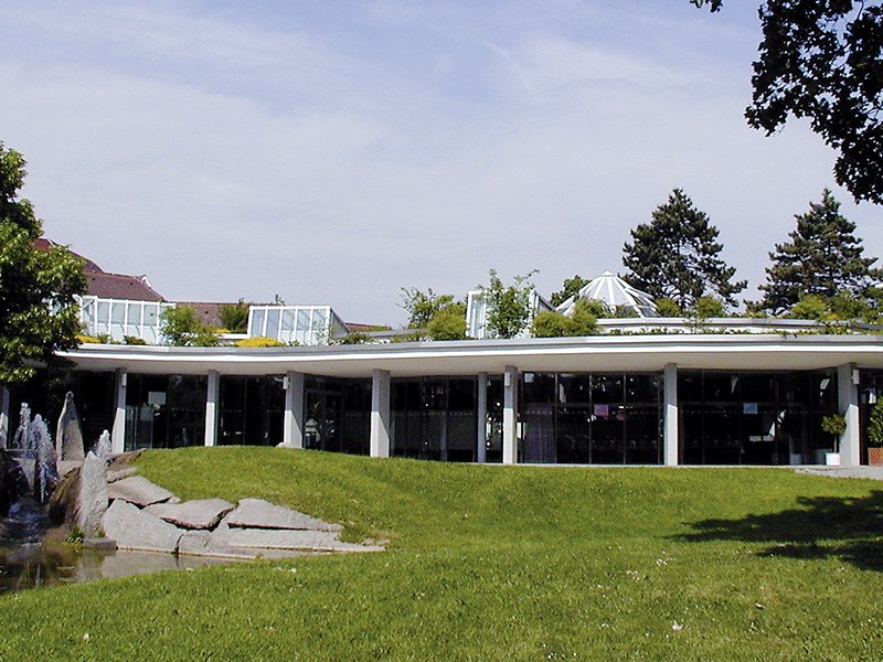 Die Stadthalle Korntal mit moderner Glasfassade und begrüntem Dach, umgeben von Rasen und Bäumen., © SK