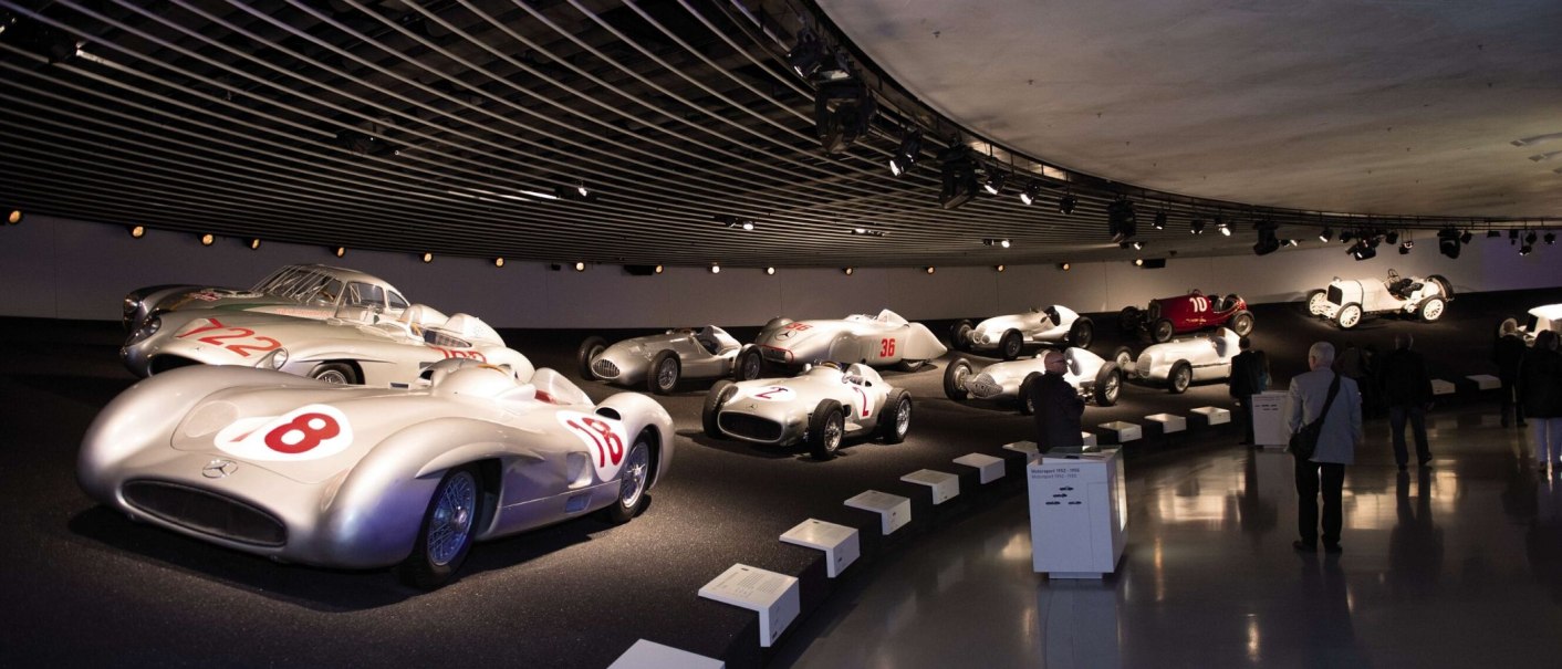 Historic Mercedes racing cars in the Mercedes-Benz Museum Stuttgart, illuminated in a modern exhibition hall with visitors in the foreground., © Stuttgart-Marketing GmbH Sebastian Berger