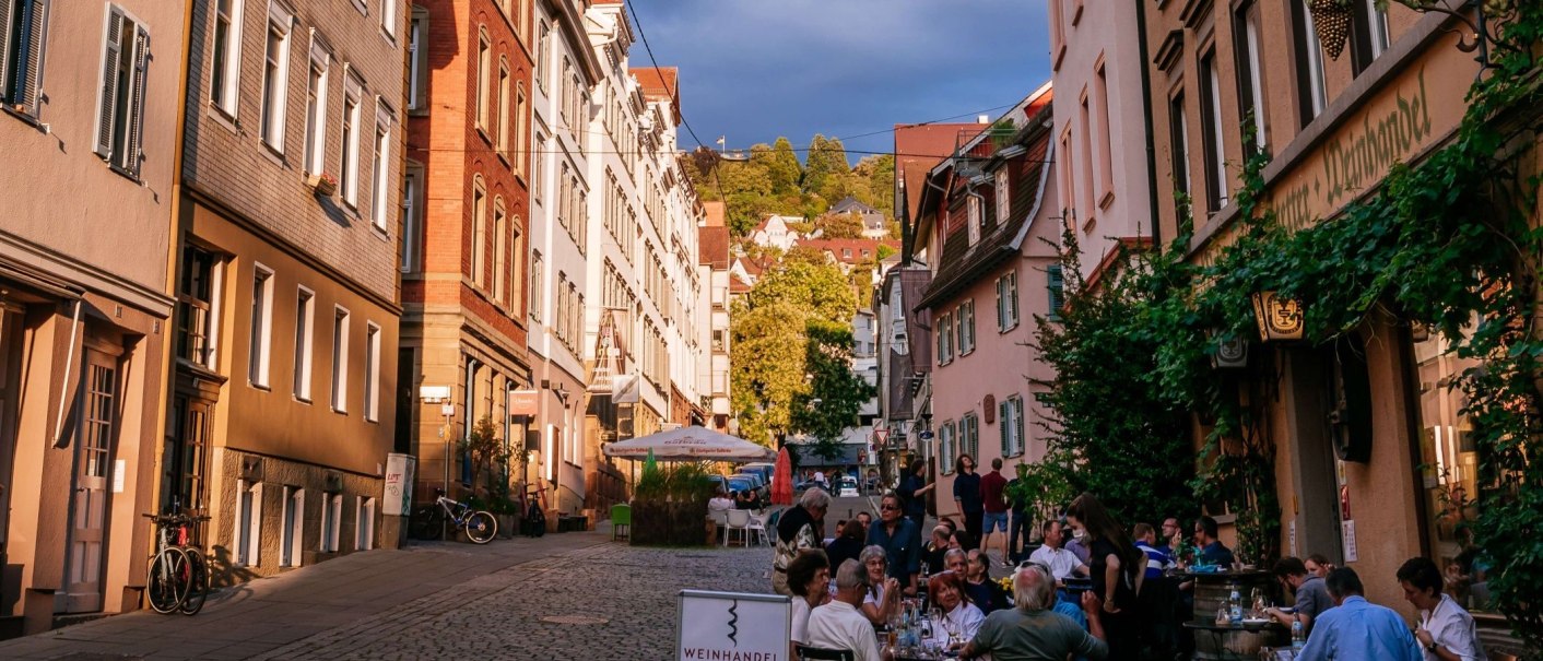 Straßenszene im Bohnenviertel mit Menschen, die in einem Café sitzen. Historische Gebäude und grüne Pflanzen säumen die Straße., © Thomas Niedermüller