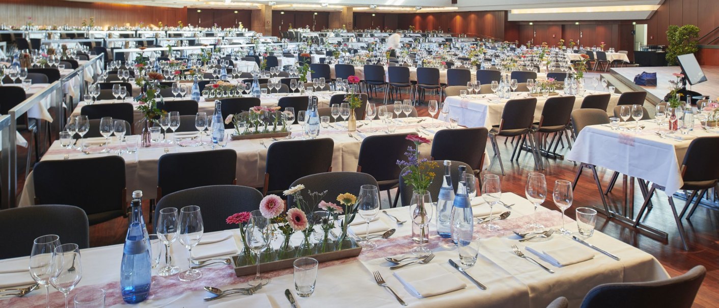 Ein großer Saal mit festlich gedeckten Tischen, Blumenarrangements und Gläsern, bereit für eine Veranstaltung., © Peter Hartung