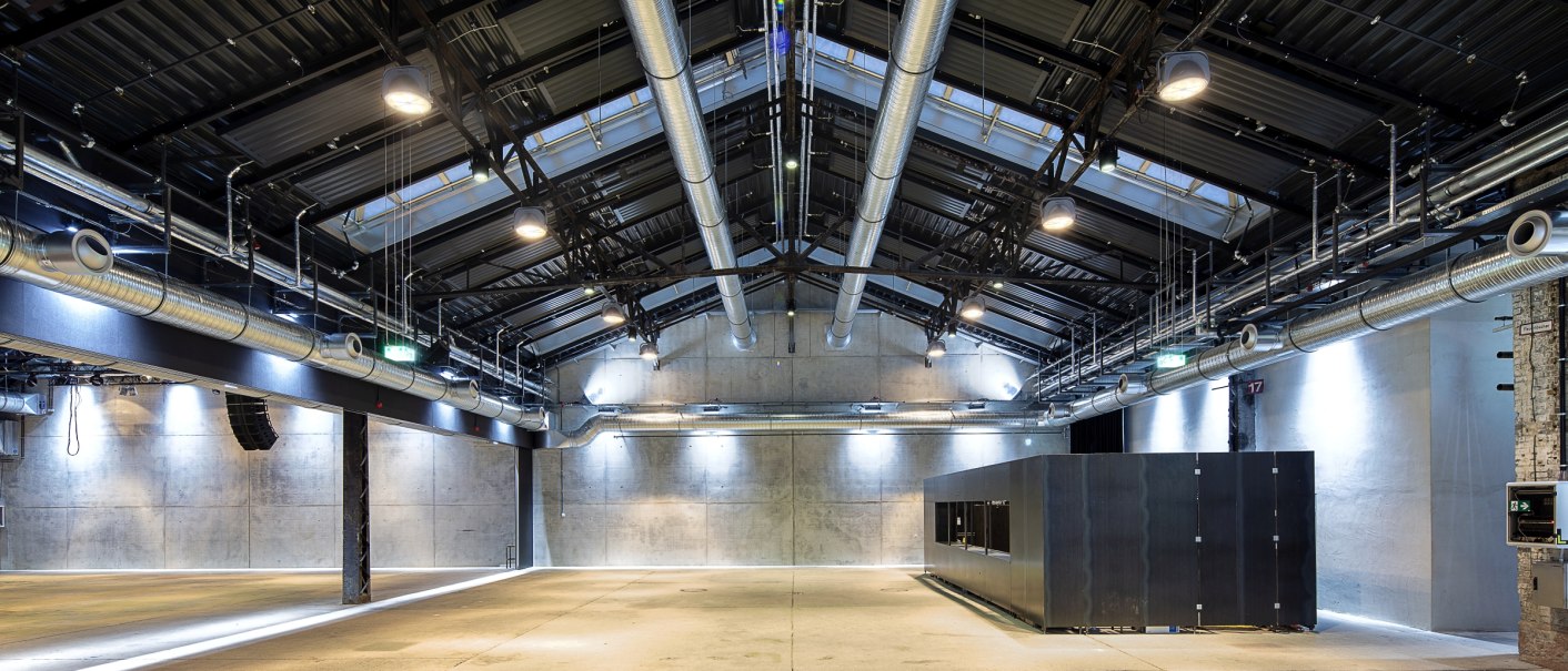Modern industrial hall with visible ventilation pipes, concrete walls and lighting. The room is empty and has a high ceiling., &copy; Wagenhallen Stuttgart GmbH & Co. KG