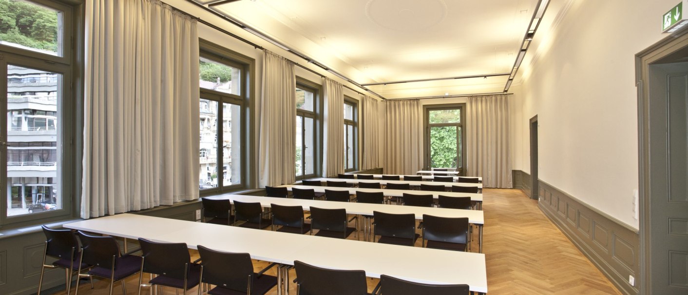 A bright conference room with white tables, black chairs, large windows and curtains. The room has a wooden floor and a high ceiling., © Forum Koenig-Karls-Bad A bright conference room with white tables, black chairs, large windows and curtains. The room has a wooden floor and a high ceiling., © Forum Koenig-Karls-Bad