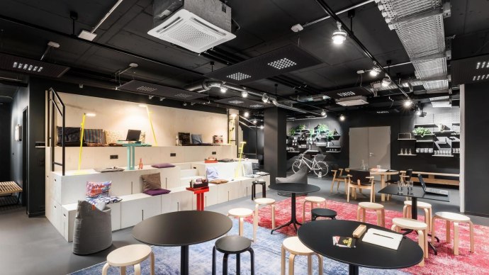 Modern lounge with black tables, light-colored stools and shelves. A bicycle hangs on the wall, plants and colorful carpets decorate the room., &copy; Design Offices GmbH