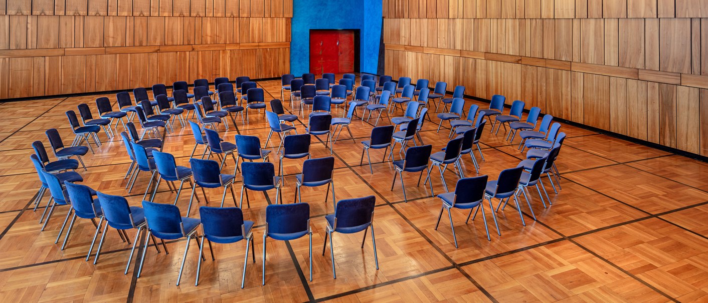 Ein Saal mit blauen Stühlen, die in konzentrischen Kreisen auf einem Holzboden angeordnet sind. Die Wände sind aus Holzpaneelen., © Kultur- und Kongresszentrum Liederhalle, Florian Selig Ein Saal mit blauen Stühlen, die in konzentrischen Kreisen auf einem Holzboden angeordnet sind. Die Wände sind aus Holzpaneelen., © Kultur- und Kongresszentrum Liederhalle, Florian Selig