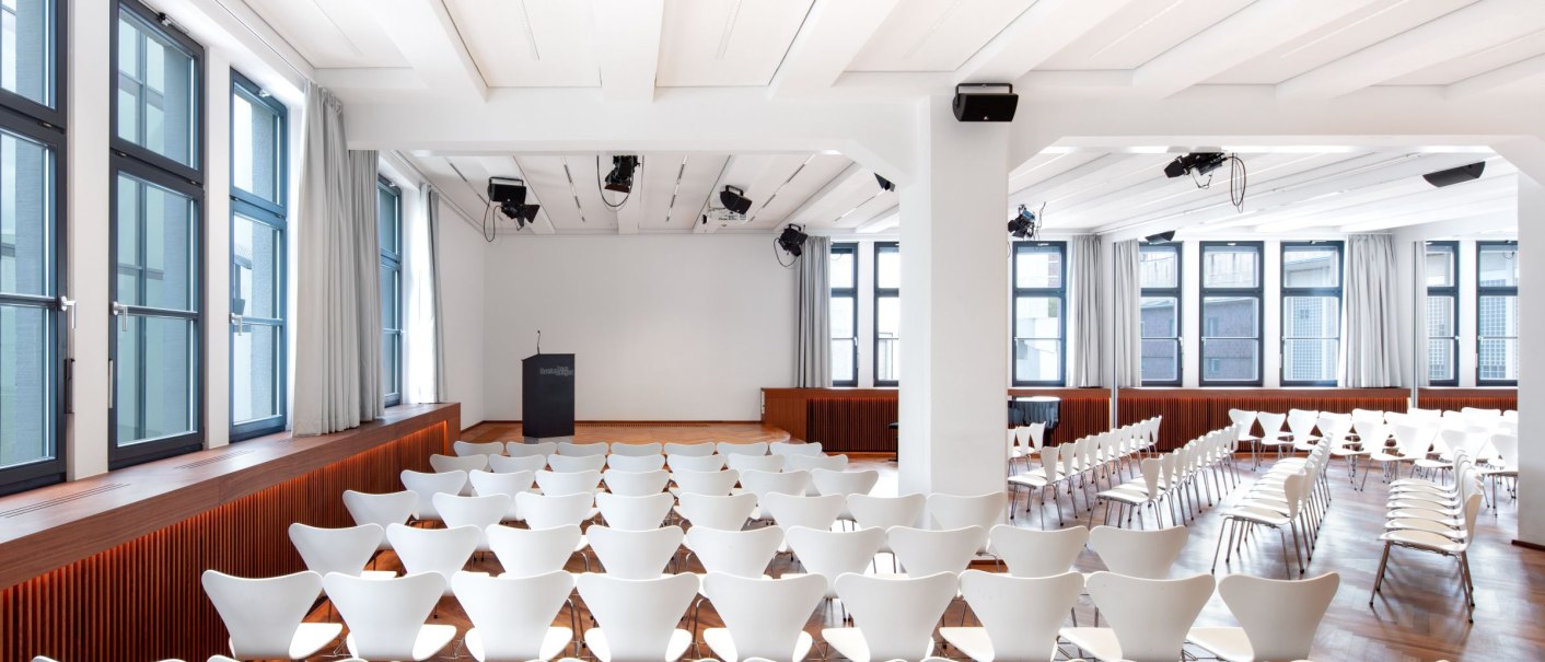 A bright conference room with white chairs, a podium and large windows. The room is empty and ready for an event., © © markus guhl fotografie