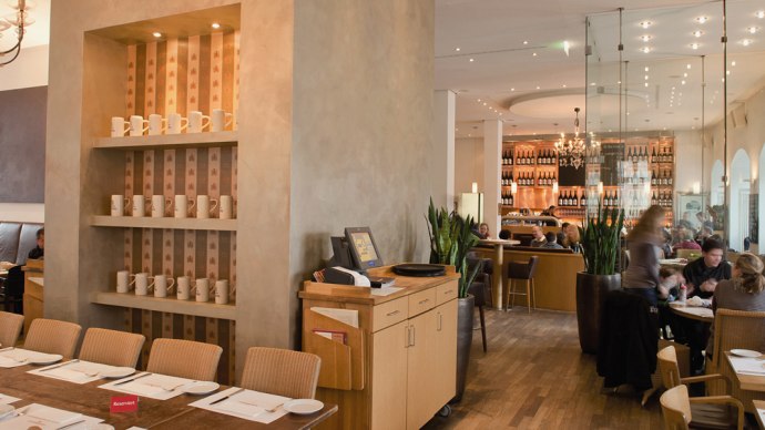 Stilvolles Restaurant mit Holzm&ouml;beln, Regalen voller Tassen und einer gem&uuml;tlichen Atmosph&auml;re. G&auml;ste sitzen an Tischen, im Hintergrund eine Bar., &copy; Aspectus Photographie Stuttgart