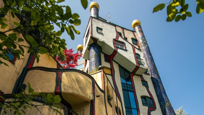 Das Hundertwasserhaus in Plochingen zeigt seine charakteristische bunte Fassade und organische Formen, umgeben von gr&uuml;nen Bl&auml;ttern und blauem Himmel., &copy; Stuttgart-Marketing GmbH, Sarah Schmid