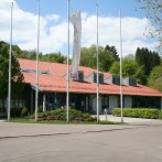 The Murrhardt town hall with its red tiled roof, surrounded by trees and flagpoles, on a sunny day., &copy; Stadt Murrhardt