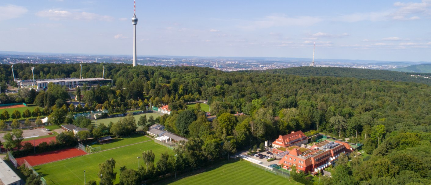 Aerial view of the Waldhotel Stuttgart, surrounded by forest, with the television tower in the background and sports fields in the foreground., © DH STUDIO Dirk Holst Aerial view of the Waldhotel Stuttgart, surrounded by forest, with the television tower in the background and sports fields in the foreground., © DH STUDIO Dirk Holst