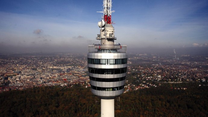Der Fernsehturm Stuttgart ragt über die Stadtlandschaft, umgeben von bewaldeten Gebieten und urbanen Strukturen unter einem klaren blauen Himmel., © Stuttgart-Marketing GmbH, Achim Mende
