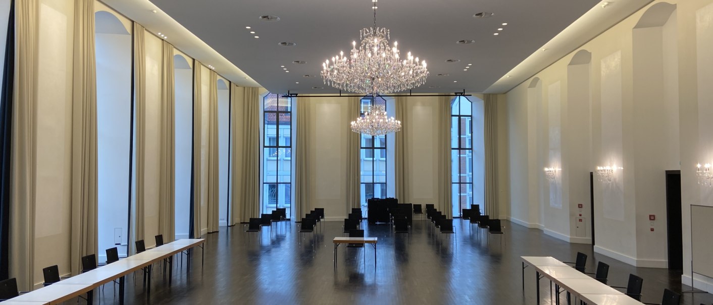 Elegant ballroom with chandeliers, long tables and chairs. High windows and bright walls create an inviting atmosphere., © Kulturzentrum Prediger