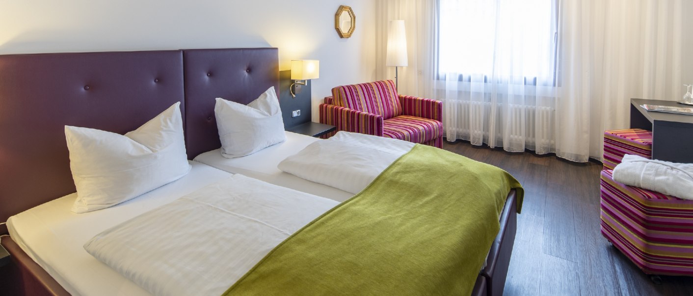 Hotel room with double bed, green blanket, striped sofa and armchair, window with curtains., &copy; Hotel Gloria