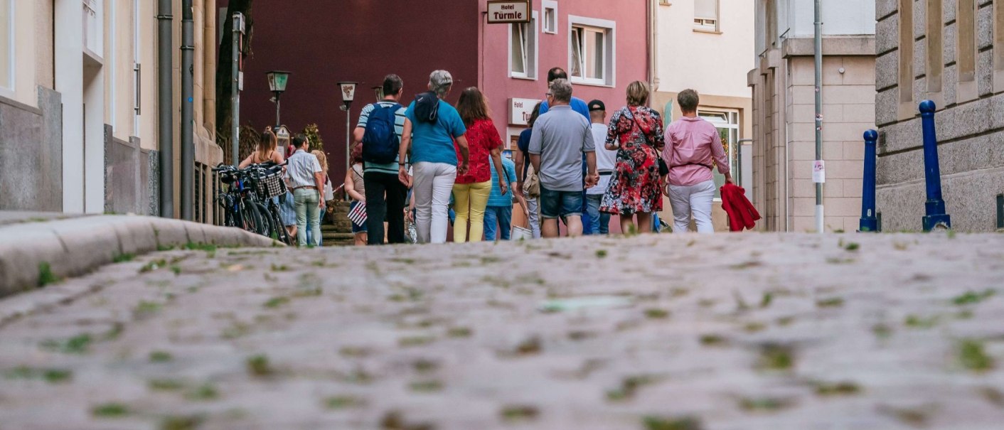 Menschen gehen auf einer gepflasterten Straße im Bohnenviertel. Im Hintergrund sind Gebäude und ein Schild mit der Aufschrift 'Hotel Türmle' zu sehen., © Thomas Niedermüller