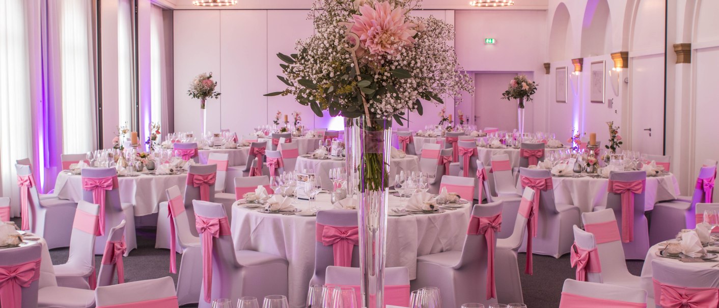 Eleganter Raum mit runden Tischen, weißen Tischdecken und rosa Stuhlschleifen, dekoriert für eine Feier im nestor Hotel Ludwigsburg., © SENDIJAREVIC.ERNES@GMAIL.COM