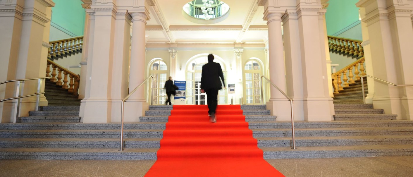 Innenansicht des Haus der Wirtschaft Baden-Württemberg mit rotem Teppich, Treppen und Säulen. Personen gehen die Treppe hinauf., © Wirtschaftministerium