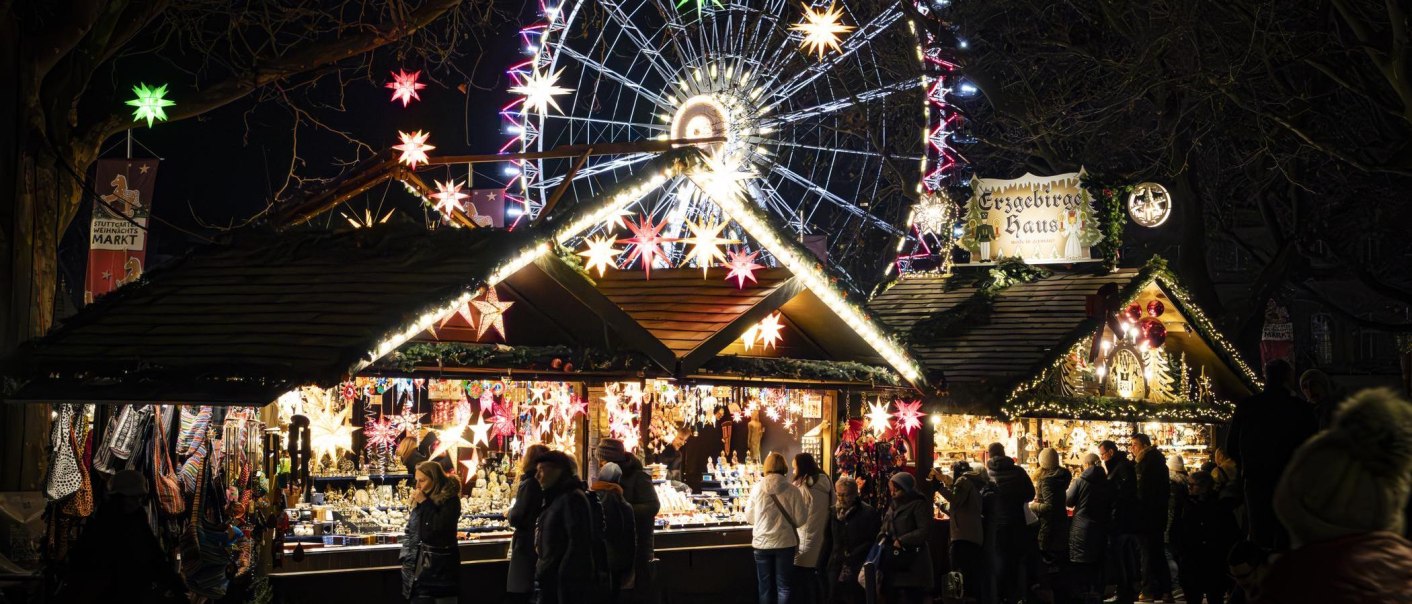 Stuttgart Christmas market at night with illuminated stalls, colorful stars and a large Ferris wheel in the background., &copy; Stuttgart-Marketing GmbH, Sarah Schmid