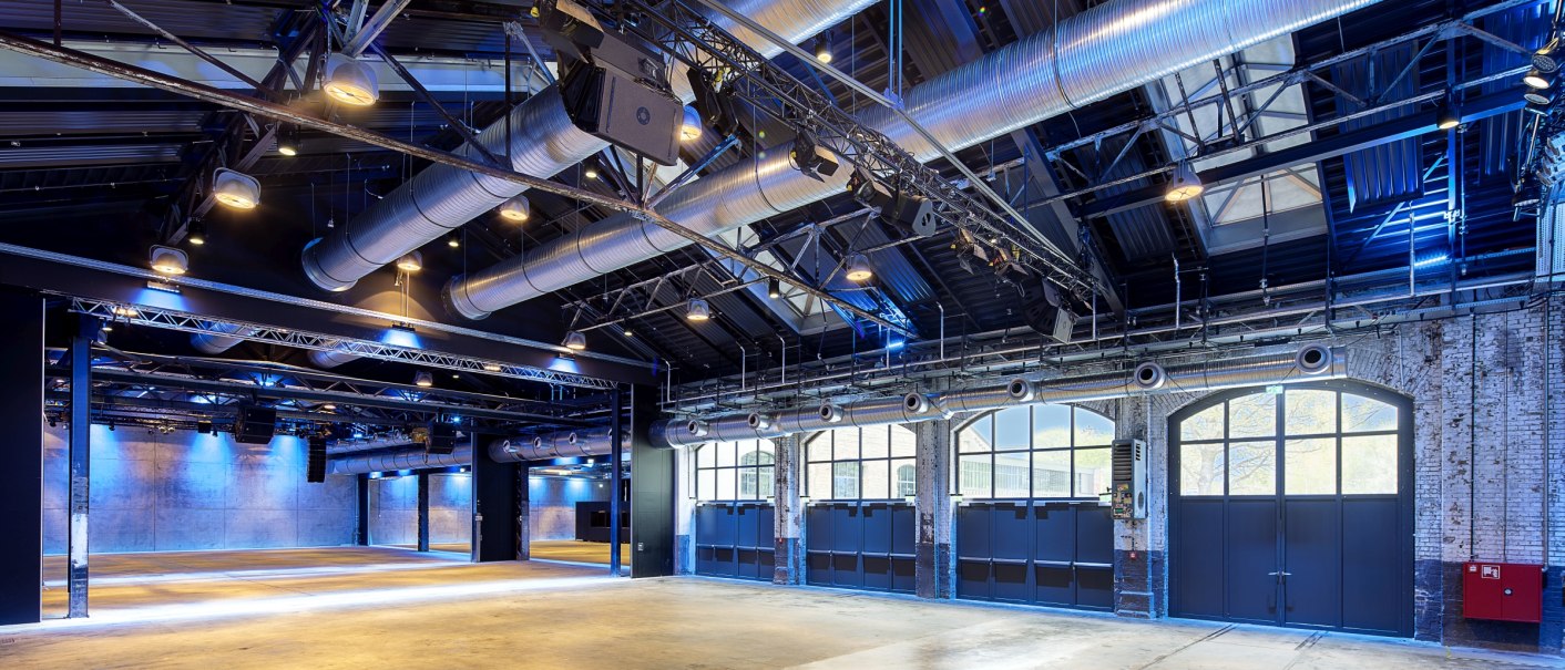 Large, modern hall with visible ventilation pipes, lighting and high windows. The floor is made of concrete, the walls of brick., © Wagenhallen Stuttgart GmbH & Co. KG