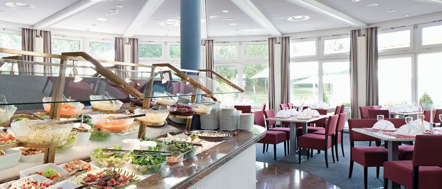 Helles Hotelrestaurant mit großem Buffet und gedeckten Tischen. Moderne Einrichtung mit roten Stühlen und großen Fenstern., © Seminaris Hotels