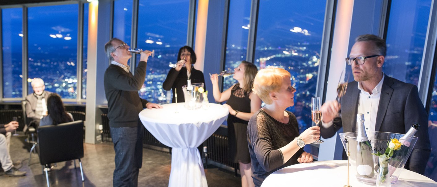 Menschen genießen Sekt in einer stilvollen Eventlocation mit Panoramablick auf die beleuchtete Stadt bei Nacht., © SWR Media Services GmbH / Alexander Fischer