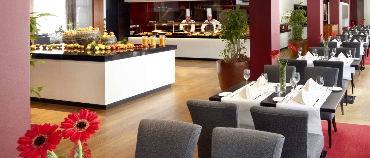 Elegantes Restaurant mit gedeckten Tischen, roten Blumen und einem Buffetbereich im Hintergrund., © Parkhotel Stuttgart Messe-Airport GmbH & Co KG Elegantes Restaurant mit gedeckten Tischen, roten Blumen und einem Buffetbereich im Hintergrund., © Parkhotel Stuttgart Messe-Airport GmbH & Co KG