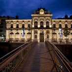 An illuminated building at night, the Forum König-Karls-Bad, with a bridge in the foreground. The sky is dark blue., © Forum Koenig-Karls-Bad