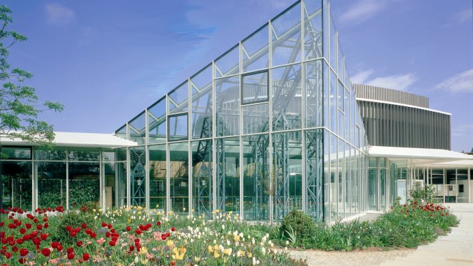 Modernes Glasgebäude der Stadthalle Sindelfingen, umgeben von bunten Blumenbeeten unter blauem Himmel., © ccbs Modernes Glasgebäude der Stadthalle Sindelfingen, umgeben von bunten Blumenbeeten unter blauem Himmel., © ccbs