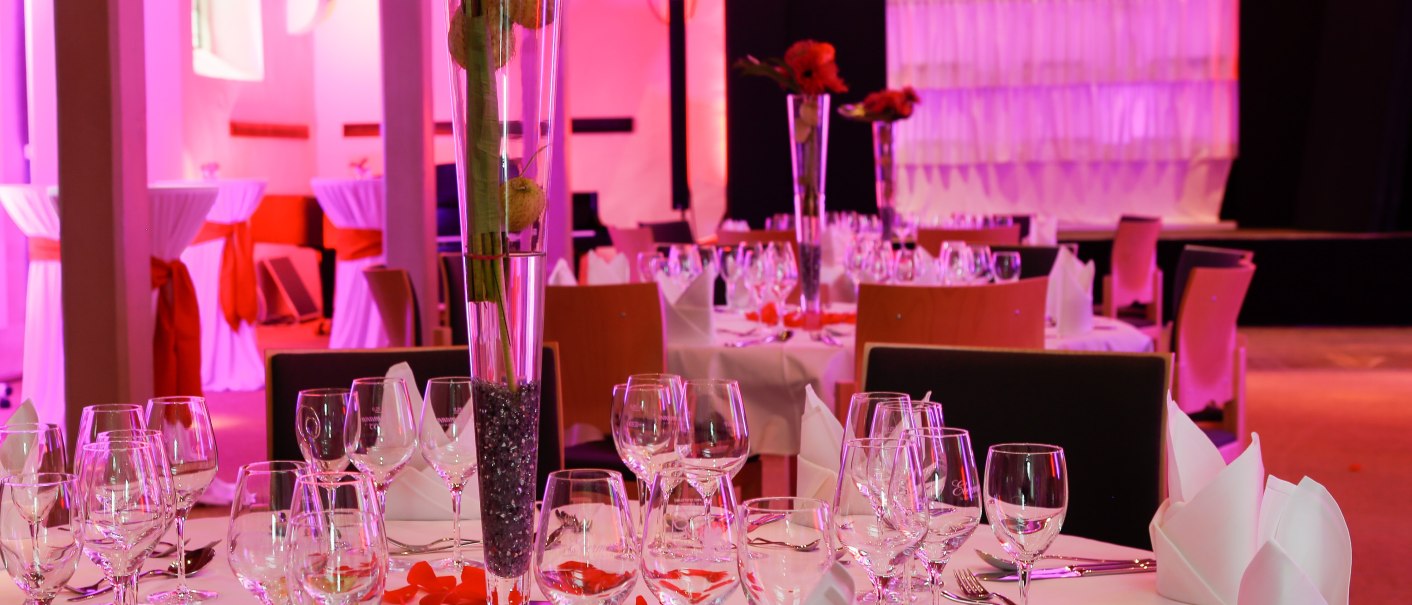 Festively laid table in the Kreuzkirche Nürtingen with flowers and glasses, colorful lighting and church windows in the background., © kkmaisch_gf Festively laid table in the Kreuzkirche Nürtingen with flowers and glasses, colorful lighting and church windows in the background., © kkmaisch_gf