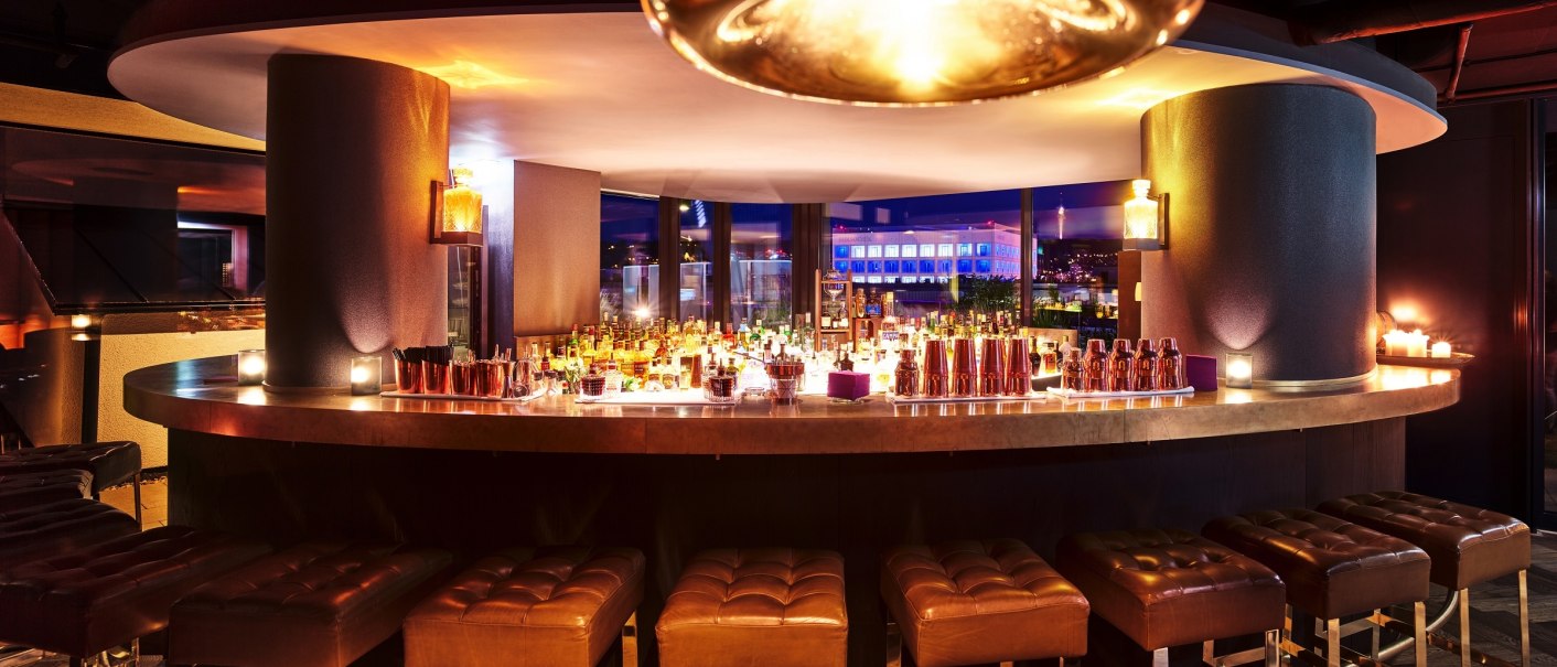 Die Wolframbar im Jaz in the City Stuttgart zeigt eine elegante, runde Bar mit beleuchtetem Tresen und stilvollen Hockern in einem modernen Ambiente., © JazHotels